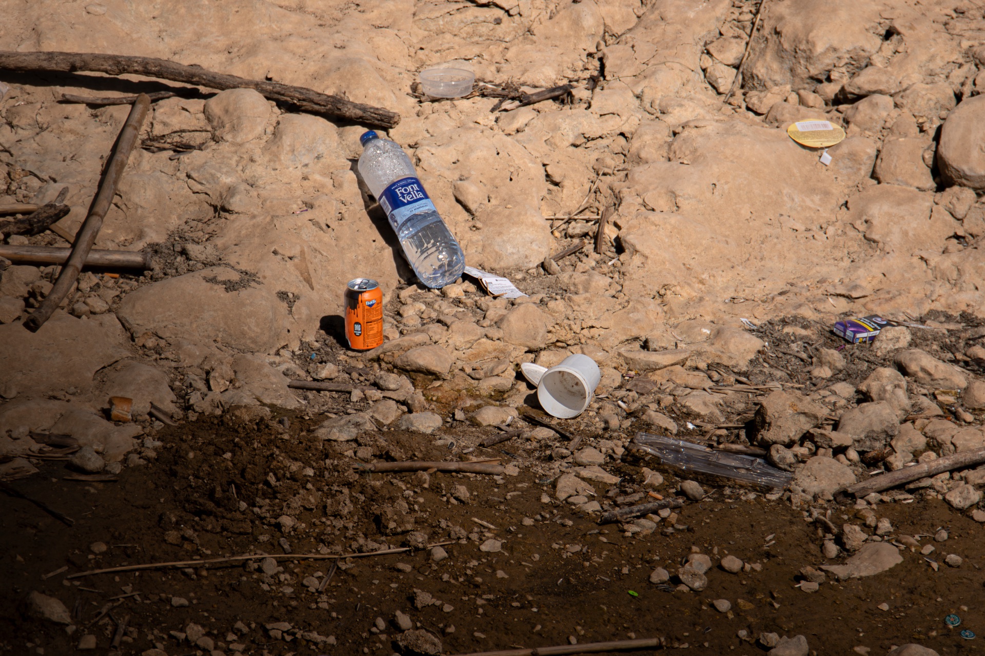 Botella, lata y otros residuos dispersos sobre un cauce seco